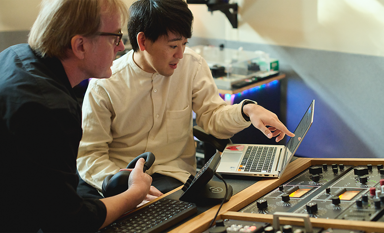 Two audio engineers reviewing sound adjustments on a laptop in a studio.