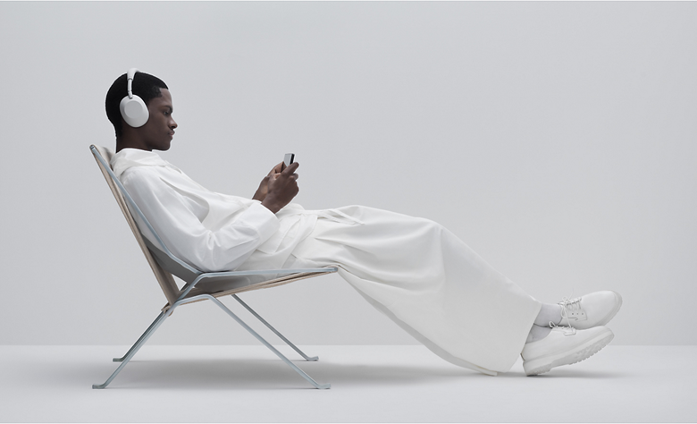 A person relaxing in a chair while using headphones and smartphone for gaming.