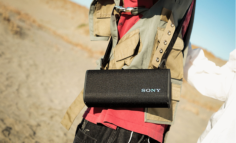 A person walking on the beach with the ULT FIELD 3 speaker hanging over their shoulder using the shoulder strap