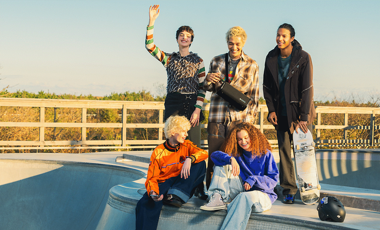Five people in a skatepark gathered around a person carrying the ULT FIELD 5 speaker across his shoulder