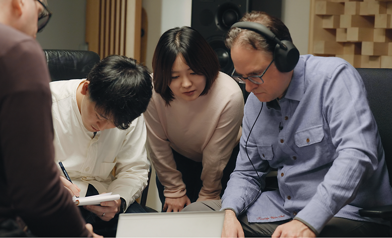 Audio engineers reviewing sound on a laptop, with one taking notes.