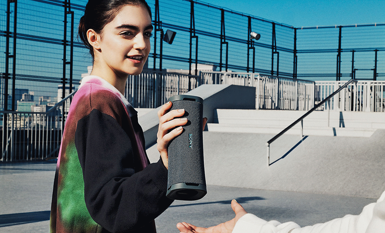 Young person handing the ULT FIELD 1 portable speaker to a friend at a skate park.