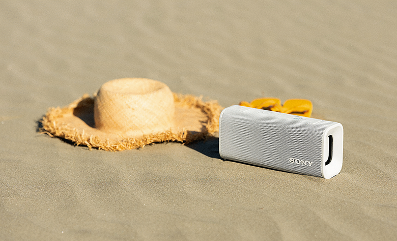 The white ULT FIELD 3 speaker sitting on the sand on a beach