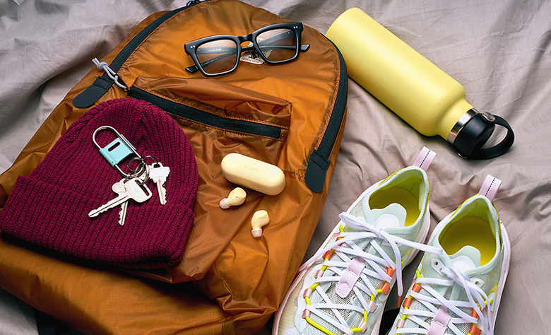 WF-C510 earbuds and respective case in yellow sat on a bed with a backpack and some personal items scattered on the bed