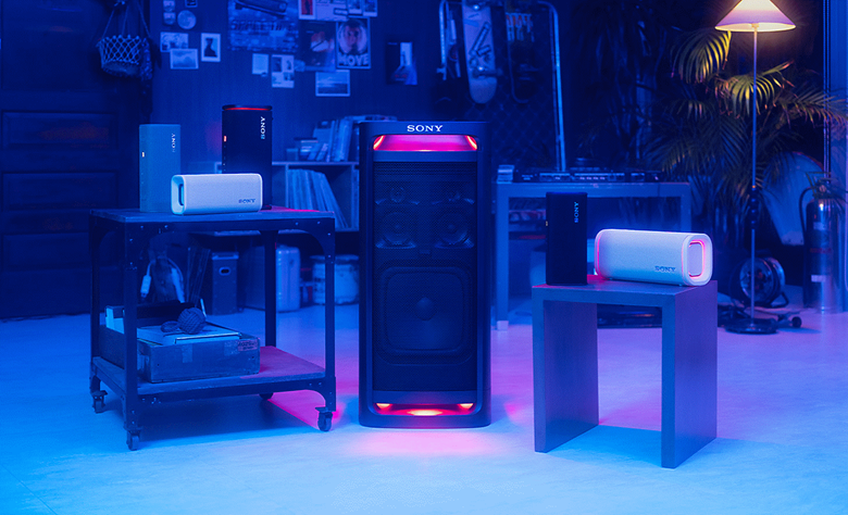 A room with a table on the left side with the ULT FIELD 3 speakers placed on top, the ULT Tower standing on the floor next to them, and then the ULT FIELD 5 speaker laying vertically on the table to the right