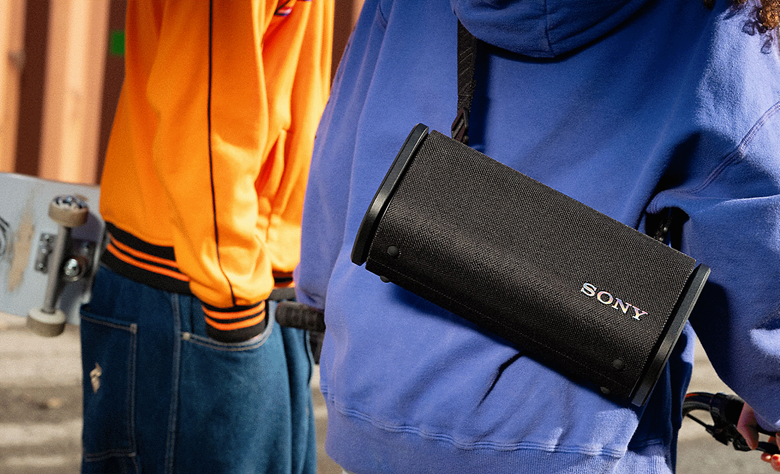 A person with their friend riding their bike  down the street with the ULT FIELD 5 hanging from the should strap across their back