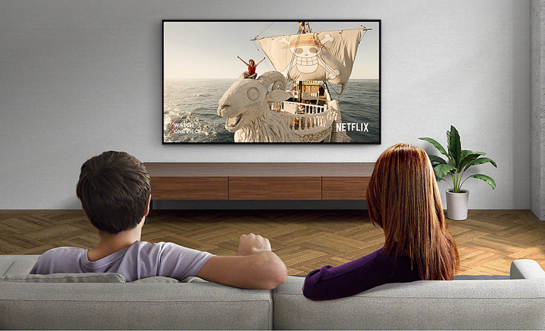 Two people sitting on a sofa watching a wall-mounted TV with screenshot of Lost in Space and Netflix logo bottom right.