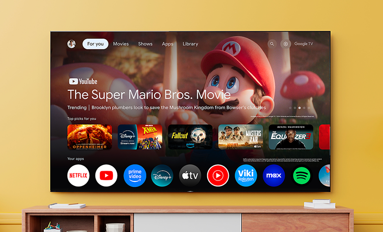 Large TV mounted on wall displaying Google TV interface, featuring The Super Mario Bros. Movie. Streaming apps shown below.
