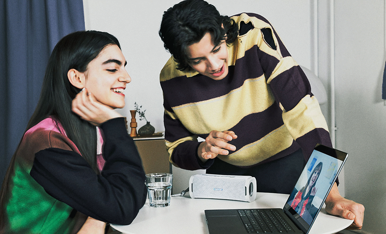 Two people making a video call on a laptop with the ULT FIELD 1 portable speaker providing the audio.