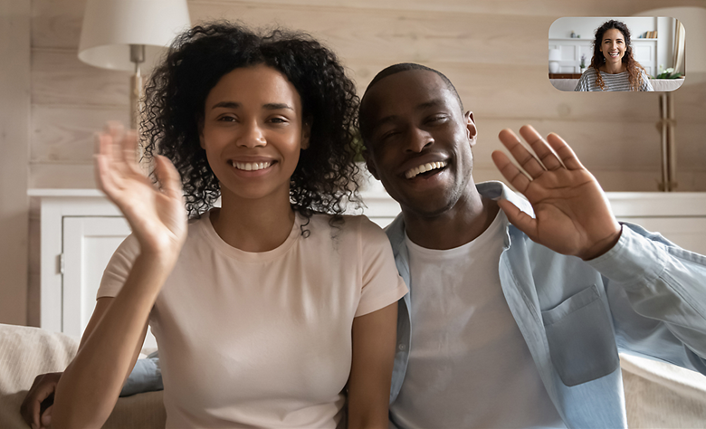 Image of couple in living room waving at a friend during video chat.